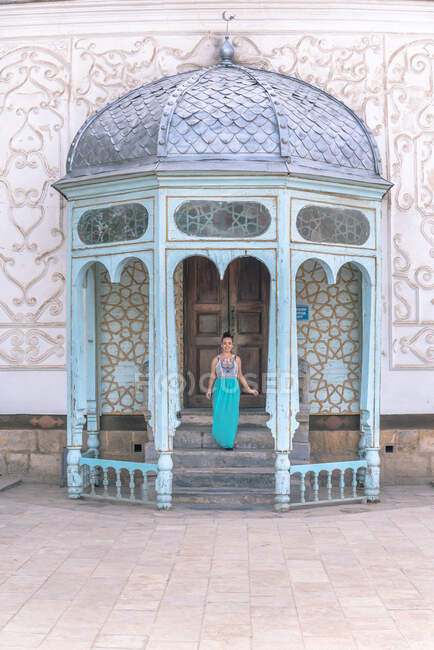 Dame en robe descendant les marches à l'extérieur du bâtiment ornemental minable par une journée ensoleillée à Boukhara, Ouzbékistan — Photo de stock