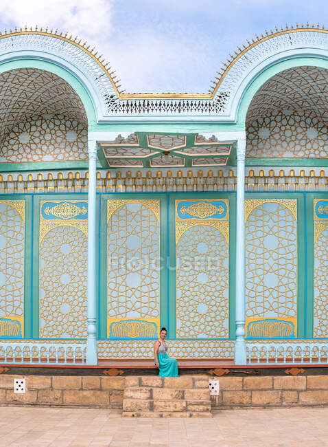 Senhora de vestido descendo degraus fora do edifício ornamental tradicional no dia ensolarado em Bukhara, Uzbequistão — Fotografia de Stock