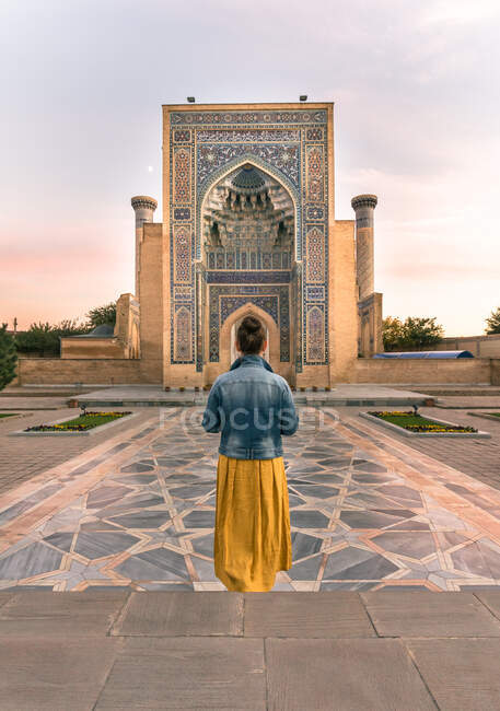 Vista trasera de una mujer irreconocible parada en la puerta de un edificio ornamental en Samarcanda, Uzbekistán - foto de stock
