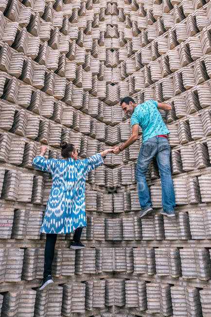 Vista posterior del hombre y la mujer étnicos tratando de escalar el muro del edificio envejecido en Bujará, Uzbekistán - foto de stock