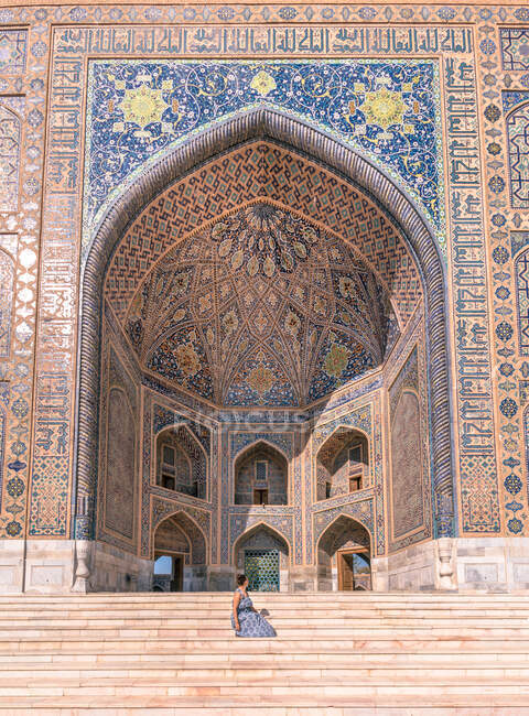 Seitenansicht einer Frau, die vor einem gewölbten ornamentalen Gebäude sitzt, während sie Registan in Samarkand, Usbekistan besucht — Stockfoto