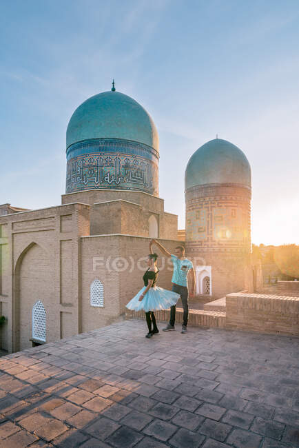 Homem e mulher de corpo inteiro dançando contra o antigo edifício islâmico com cúpulas enquanto visitam Shah-i-Zinda em Samarcanda, Uzbequistão — Fotografia de Stock