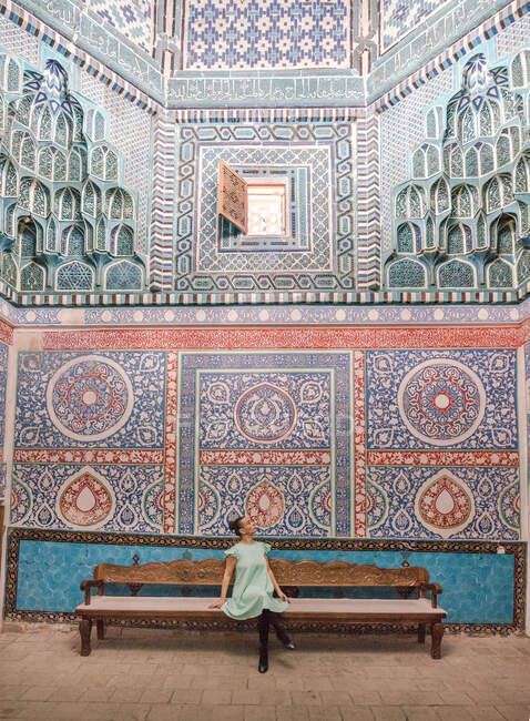Frau sitzt in einer rustikalen traditionellen Bank und bewundert Ornamente an Wänden eines alten Gebäudes, während sie Samarkand, Usbekistan besucht — Stockfoto