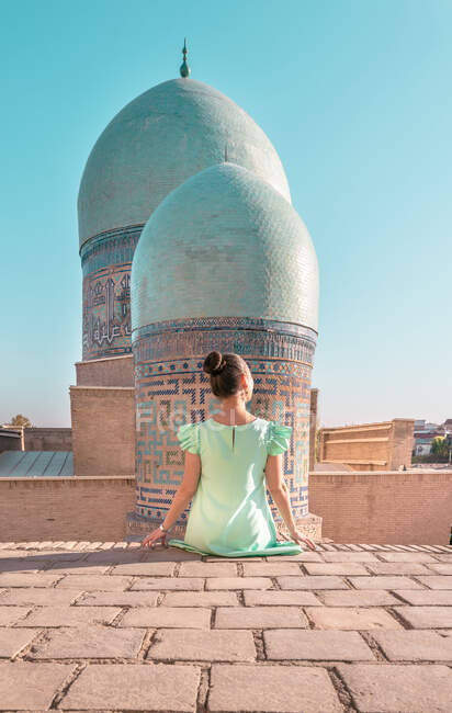 Visão traseira da mulher anônima sentada no prédio antigo contra cúpulas de Shah-i-Zinda no dia ensolarado em Samarcanda, Uzbequistão — Fotografia de Stock