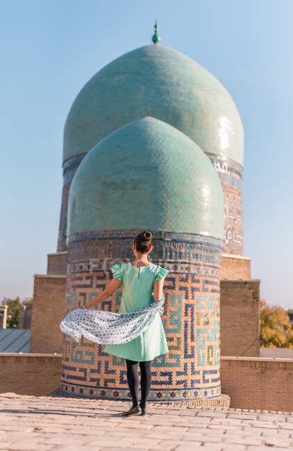 Visão traseira da mulher anônima em pé no prédio antigo contra cúpulas de Shah-i-Zinda no dia ensolarado em Samarcanda, Uzbequistão — Fotografia de Stock