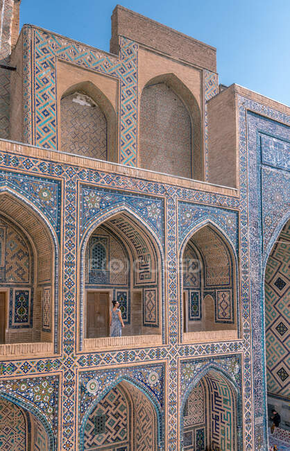 Подорожуюча жінка йде на терасі аркової ісламської будівлі з синіми прикрасами під час відвідування штату Самарканд (Узбекистан). — стокове фото