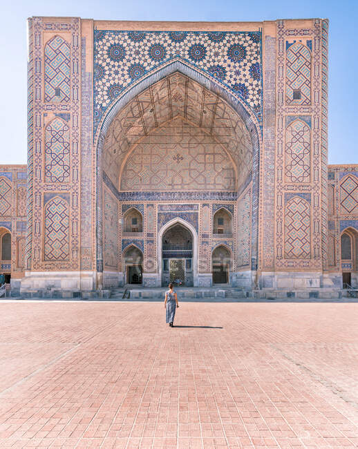 На задньому плані нерозпізнана жінка стоїть у дверях обшарпаного декоративного будинку Регістан у Самарканді (Узбекистан). — стокове фото