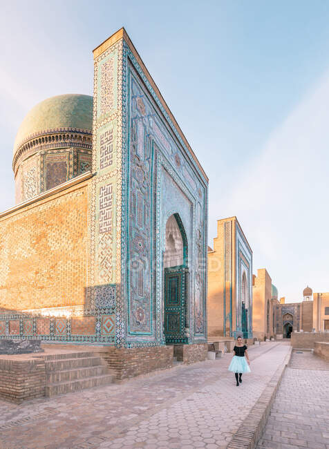 Promenade touristique féminine sur le trottoir près du bâtiment ornemental vieilli de la nécropole de Shah-i-Zinda par une journée ensoleillée à Samarkand, en Ouzbékistan — Photo de stock