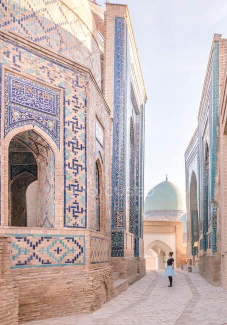 Promenade touristique féminine sur le trottoir près du bâtiment ornemental vieilli de la nécropole de Shah-i-Zinda par une journée ensoleillée à Samarkand, en Ouzbékistan — Photo de stock