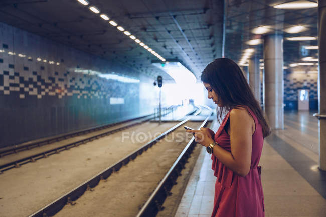 Mujer de pelo largo con smartphone de pie en la estación de metro de Budapest - foto de stock