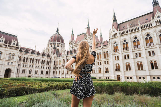 Back view of woman looking at ancient amazing old building with towers and domes and raising hand in Budapest — Stock Photo