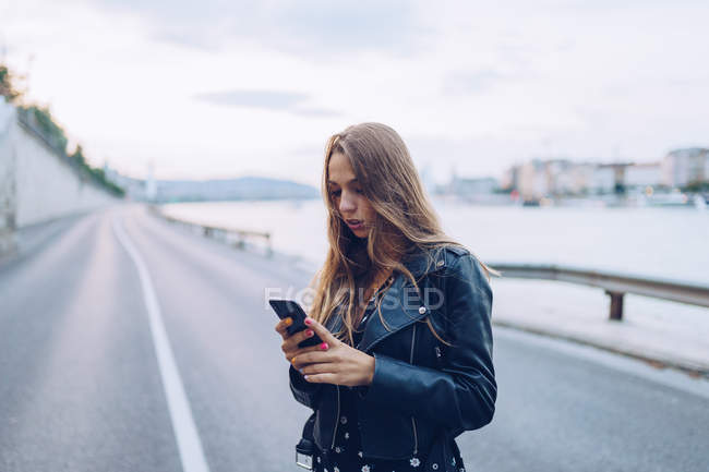 Femme élégante aux cheveux longs naviguant sur smartphone à Budapest — Photo de stock