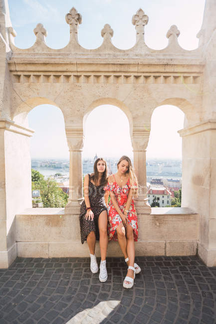 Cheerful trendy girl friends on stone designed window with columns in balcony of ancient building in Budapest — Stock Photo
