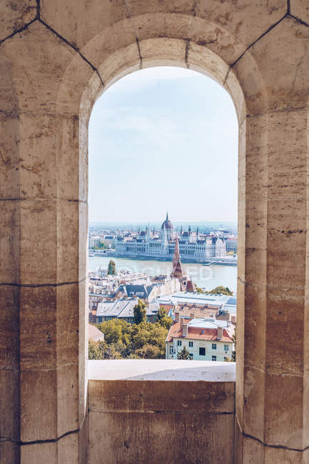 Antica finestra squallida che si affaccia pittoresco paesaggio sulla città e il fiume calmo sotto il cielo luminoso a Budapest — Foto stock
