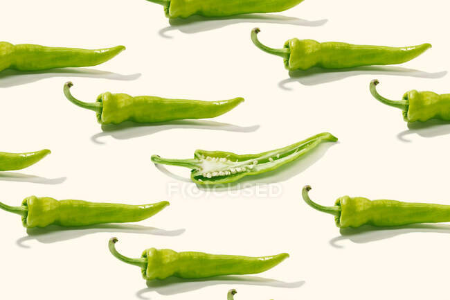 From above creative composition of sliced green pepper with seeds among whole peppers on white surface — Stock Photo