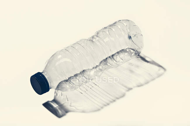 Вид збоку порожня пластикова пляшка з синьою шапочкою з контрастною тінь на білій поверхні — стокове фото