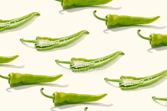 De acima mencionada composição criativa de pimentão verde fatiado com sementes entre pimentas inteiras na superfície branca — Fotografia de Stock