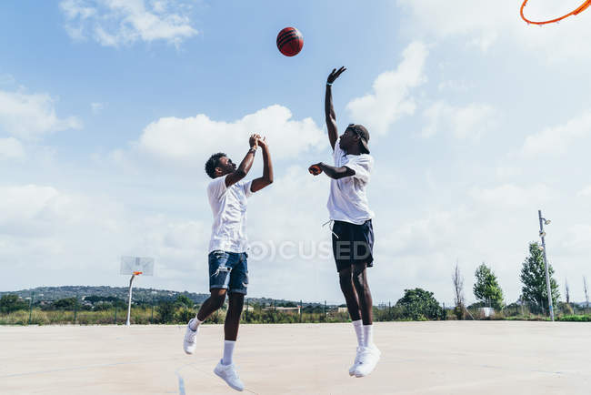 Vista lateral de chicos afroamericanos jugando baloncesto en día brillante en el patio de recreo - foto de stock