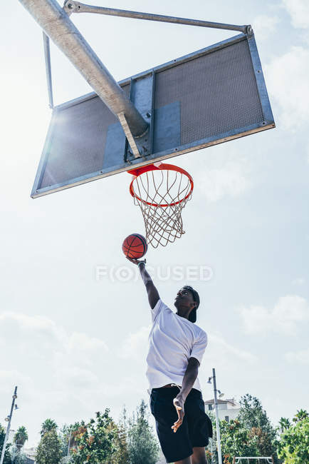 Мощный и энергичный афроамериканский спортсмен, висящий на баскетбольном круге после забивания мяча в сетке на детской площадке — стоковое фото