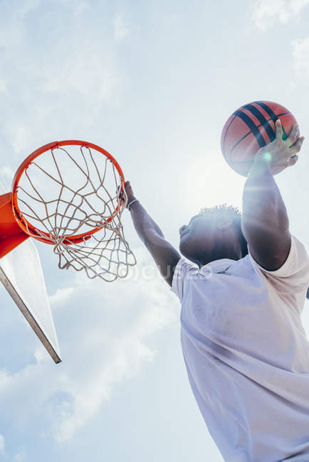 Poderoso atleta afro-americano enérgico pendurado na volta de basquete depois de marcar bola na rede no playground — Fotografia de Stock