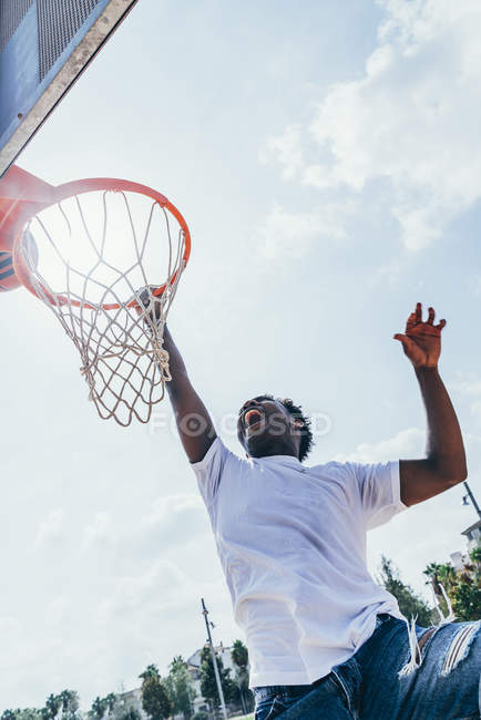 Potente energico sportivo afroamericano appeso sul giro di basket dopo aver segnato palla in rete sul parco giochi — Foto stock