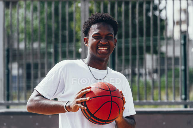 Jogador afro-americano alegre segurando bola laranja e olhando para a câmera com sorriso largo — Fotografia de Stock