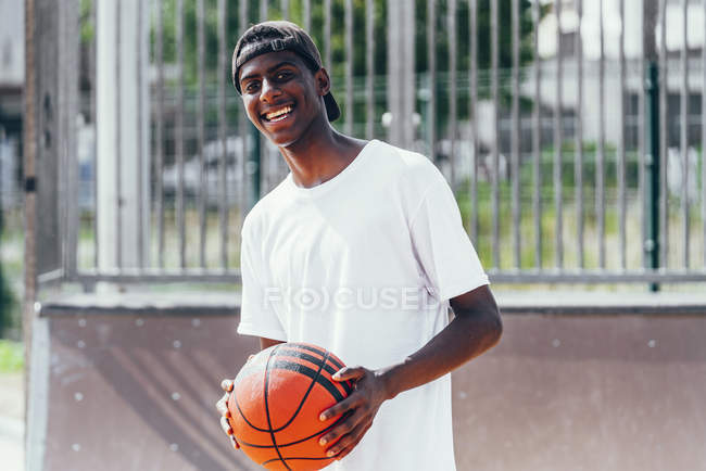 Веселый афроамериканец держит оранжевый мяч и смотрит в камеру с широкой улыбкой — стоковое фото