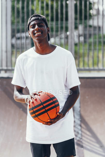 Jogador afro-americano alegre segurando bola laranja e olhando para a câmera com sorriso largo — Fotografia de Stock