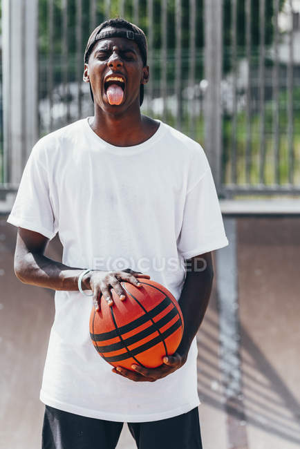Fröhlicher afrikanisch-amerikanischer Spieler mit orangefarbenem Ball und mit ausgestreckter Zunge und breitem Lächeln in die Kamera — Stockfoto