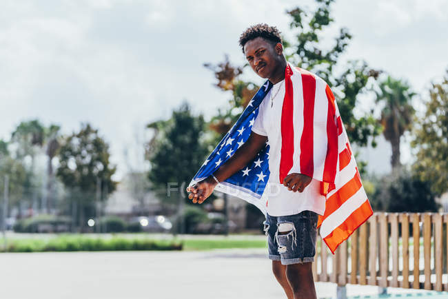 Серьезный афроамериканец, держащий американский флаг на плече и отворачивающийся — стоковое фото