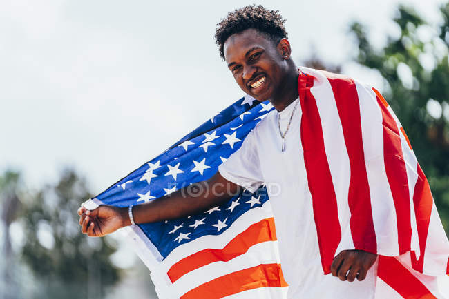 Homem afro-americano sério segurando bandeira americana no ombro e olhando para longe — Fotografia de Stock