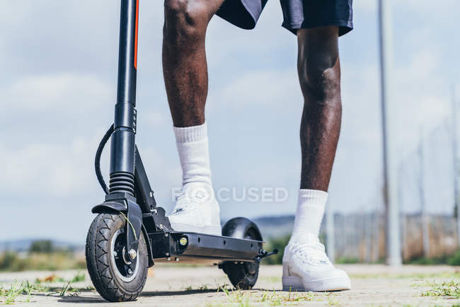 Immagine ritagliata di uomo sportivo afroamericano cavalcando su scooter elettrico in giornata nuvolosa luminosa — Foto stock