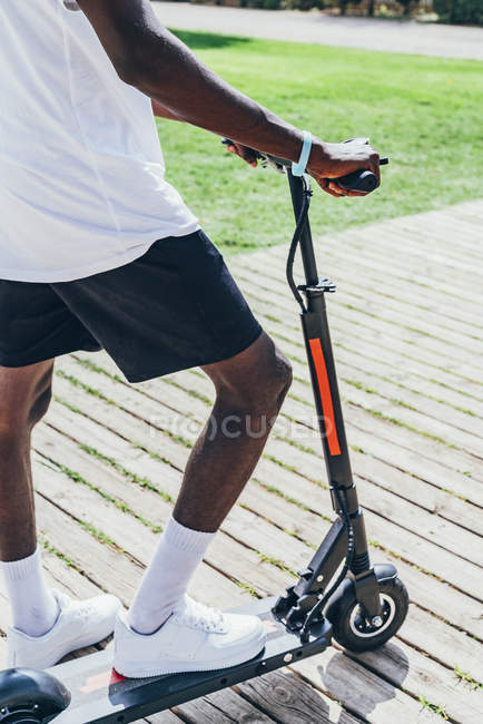 Imagen recortada de hombre deportivo afroamericano montando en scooter eléctrico en día nublado brillante - foto de stock