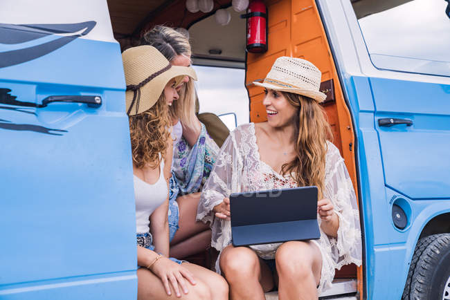 Charming long-haired women in summer wear browsing tablet and talking with smile sitting in car salon — Stock Photo