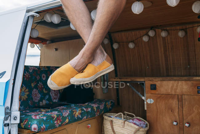 Las piernas del hombre en zapatos de tela amarilla colgando del techo del coche en el día brillante - foto de stock