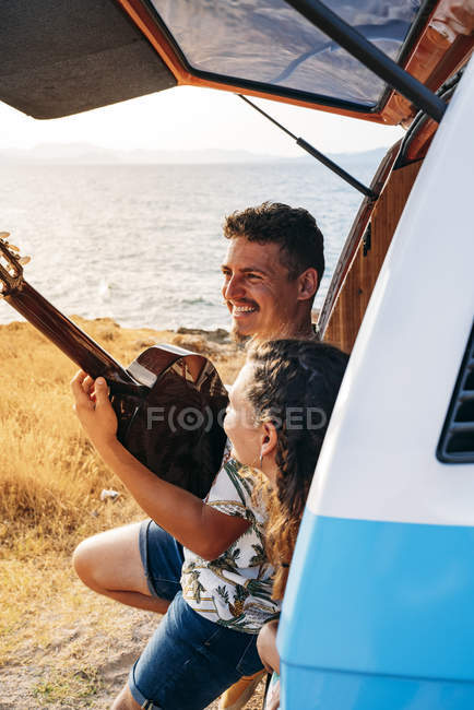 Cheerful tender couple in trunk of car having fun together playing on guitar and enjoying music — Stock Photo