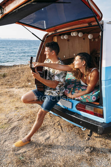 Fröhlich zartes Paar im Kofferraum des Autos, das zusammen Spaß hat, Gitarre spielt und Musik genießt — Stockfoto