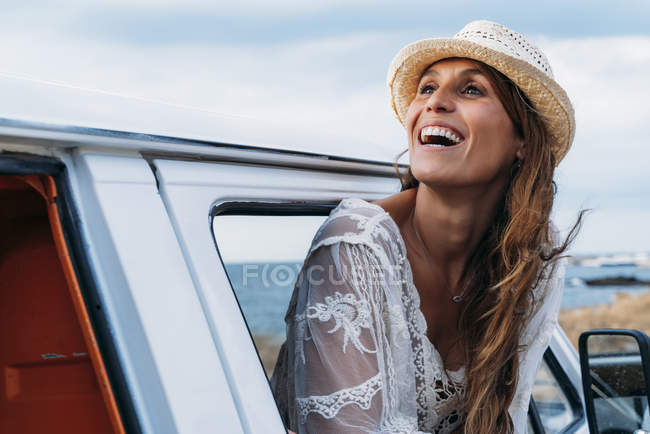 Agréable charmante dame au chapeau regardant loin avec sourire tout en ouvrant la porte de la voiture sur la plage — Photo de stock