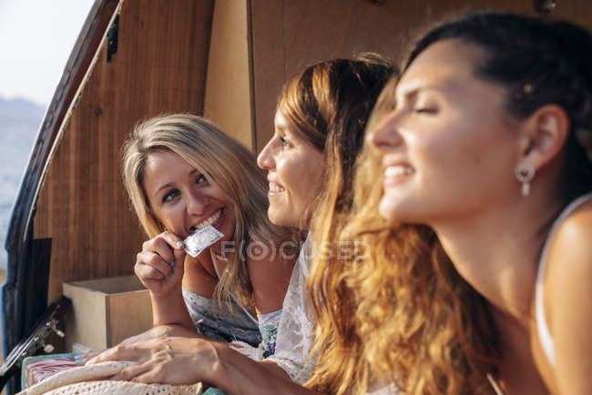 Joyful female friends discussing and showing condom in trunk of car — Stock Photo