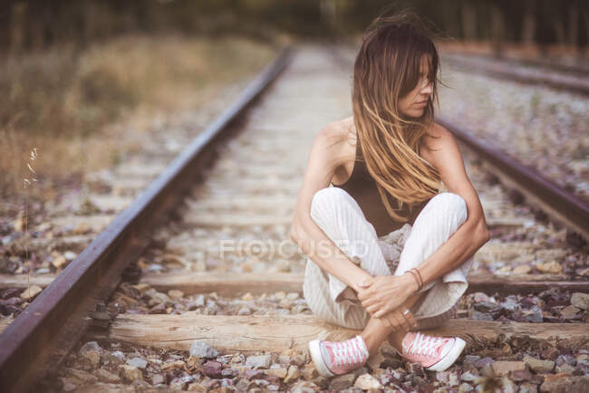 Mulher de cabelos compridos sentada em ferrovias cobertas de grama seca — Fotografia de Stock