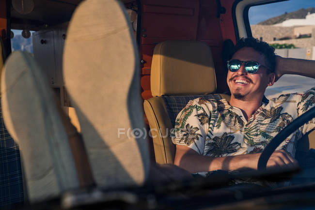 Heureux homme adulte assis dans un van avec les jambes sur le tableau de bord dans la voiture garée — Photo de stock
