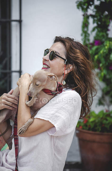 Happy woman cuddling dog while resting together on fence of flowerbed with tropical plants in Marbella — Stock Photo