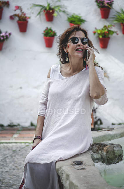 Trendy concentrated woman in sunglasses talking on mobile phone while sitting on Marbella street — Stock Photo