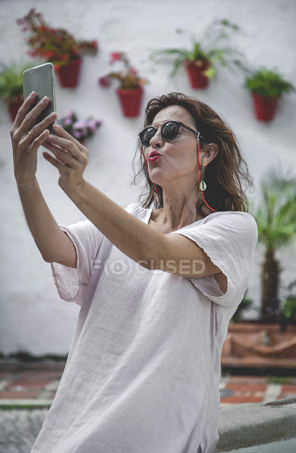 Trendy outgoing woman in sunglasses taking selfie on mobile phone on Marbella street — Stock Photo