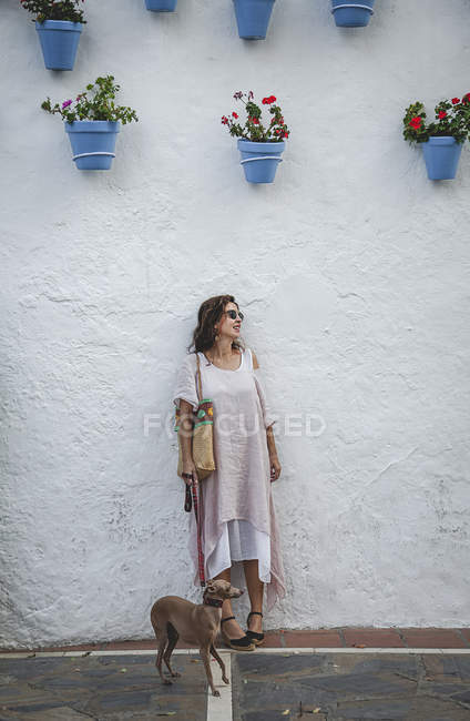 Optimistic happy woman leaning on wall in Marbella and holding greyhound dog on leash — Stock Photo