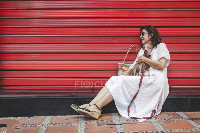 Vista laterale della donna allegra soddisfatta coccolando cane carino mentre si rilassa vicino alla parete a strisce rosse urbane in provincia di Spagna — Foto stock