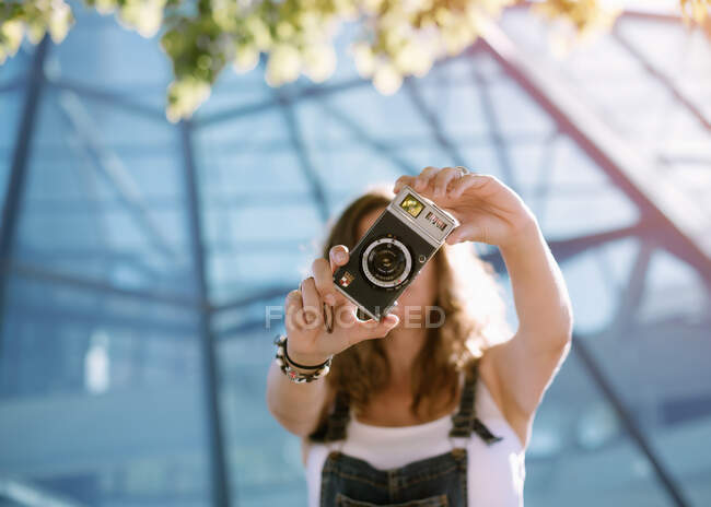 Jovem mulher entusiasta captura momento tirar foto na câmera no fundo da arquitetura de vidro — Fotografia de Stock