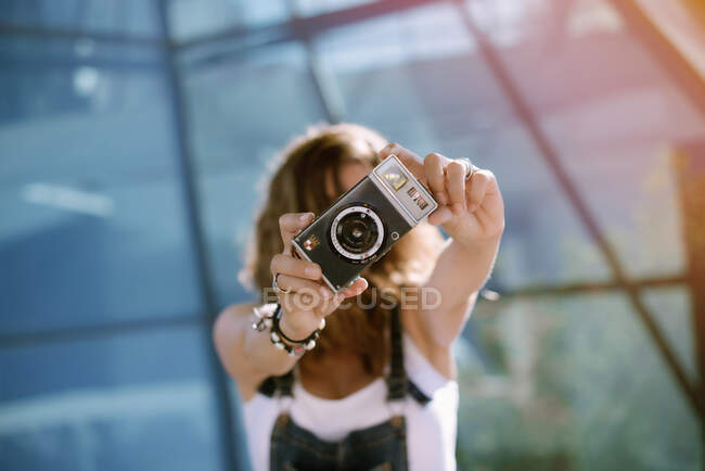 Joven mujer entusiasta capturando momento tomando fotos en la cámara en el fondo de la arquitectura de vidrio - foto de stock