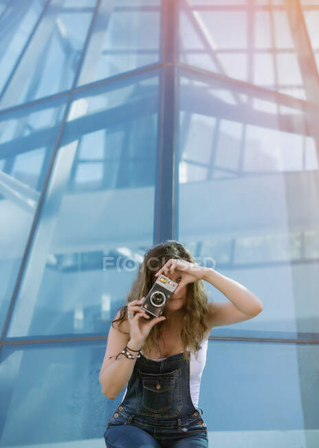 Jovem mulher entusiasta captura momento tirar foto na câmera no fundo da arquitetura de vidro — Fotografia de Stock