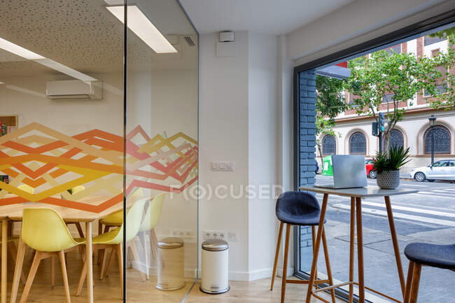 Moderno design interno di luce spazioso ufficio zonata da parete di vetro con comode sedie gialle e sgabelli da bar grigi a tavoli di legno — Foto stock